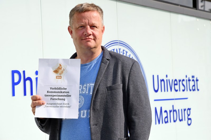 Gert Bange mit dem Siegel vor dem Uni-Verwaltungsgebäude