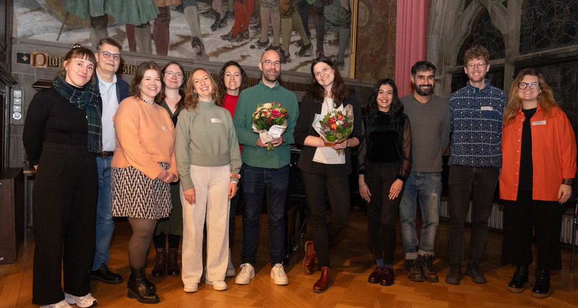 Die Preisträger des Preises für exzellente Promotionsbegleitung 2024 (Bildmitte, mit Blumenstrauß) Dr. Felix Anderl (links) und Dr. Anke Haberkamp (rechts), zusammen mit Prof. Dr. Sabine Pankuweit sowie Promovierenden und PostDocs bei der Preisverleihung.