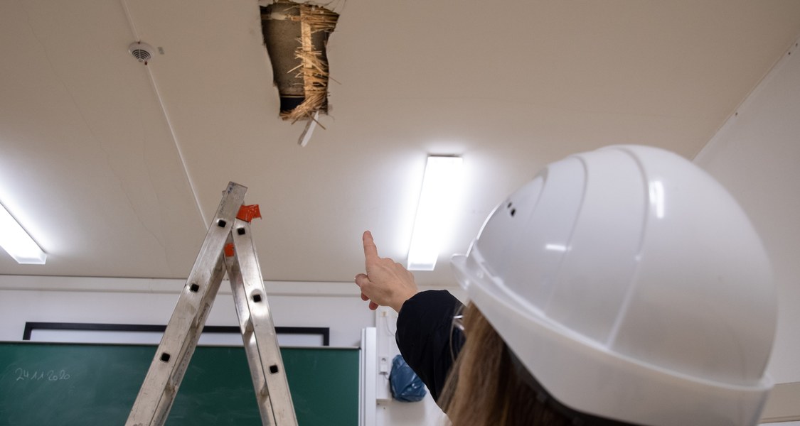 Person - von hinten aufgenommen - zeigt auf geöffnete Unterdecke in einem Büro