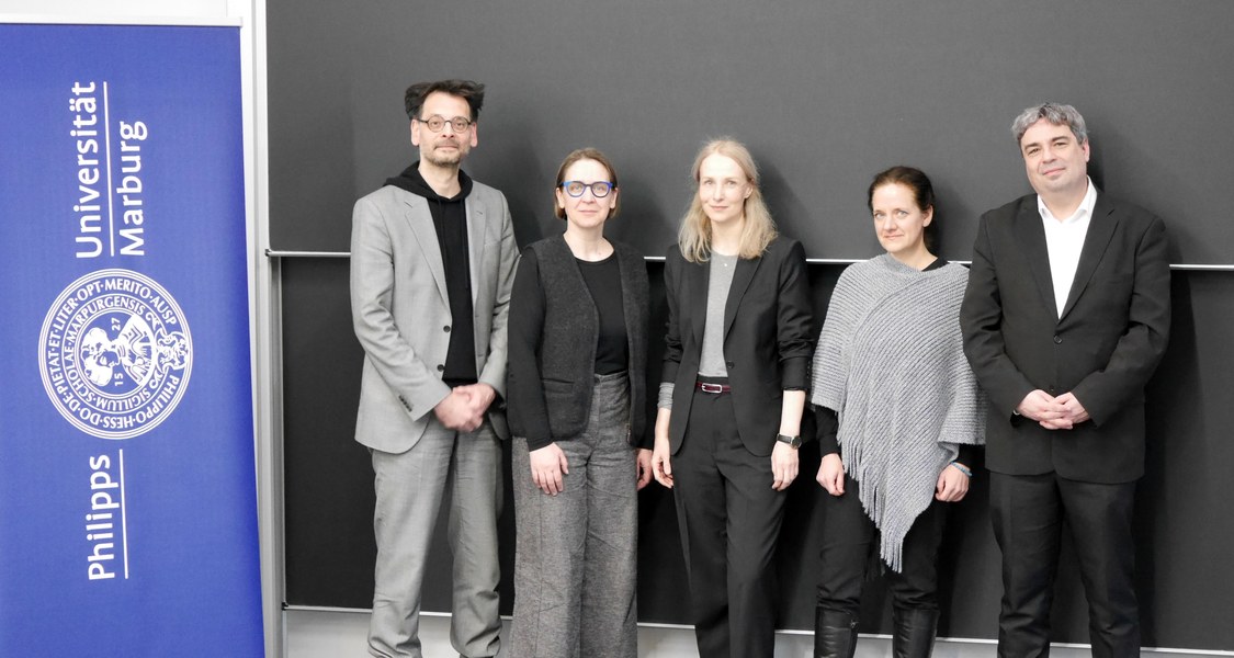 Gruppenbild, sechs Personen neben dem Logo der Universität Marburg