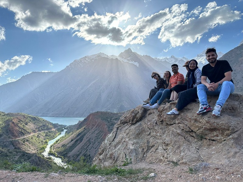 Eine Gruppe Studierender sitzen auf einer Felsenkuppe vor einem weiten Bergpanorama