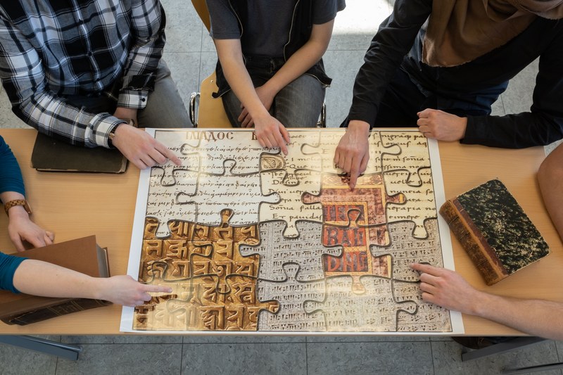 Posterausdruck des IKSL-Puzzle auf dem Tisch mit Wörterbüchern und Händen