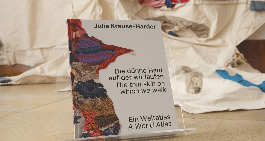 Vor der textilen Weltkarte von Julia Krause-Harder steht ihr neues Künstlerbuch