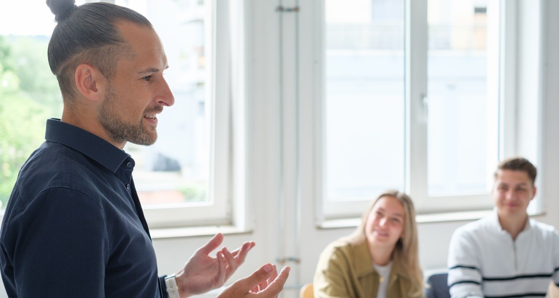 Talentscout Jonathan spricht im Unterrichtsraum zu einer Gruppe Schüler*innen