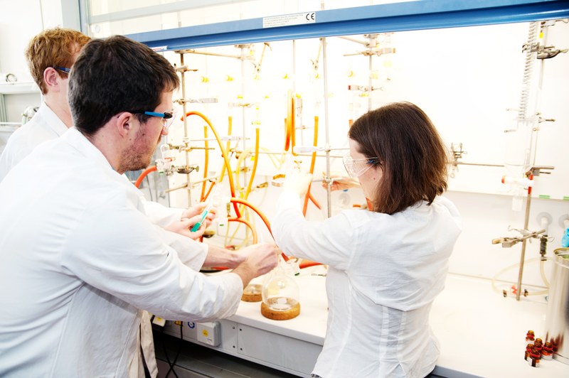 Chemie-Studierende in einem Labor: Sie tragen weiße Kittel und Schutzbrillen.