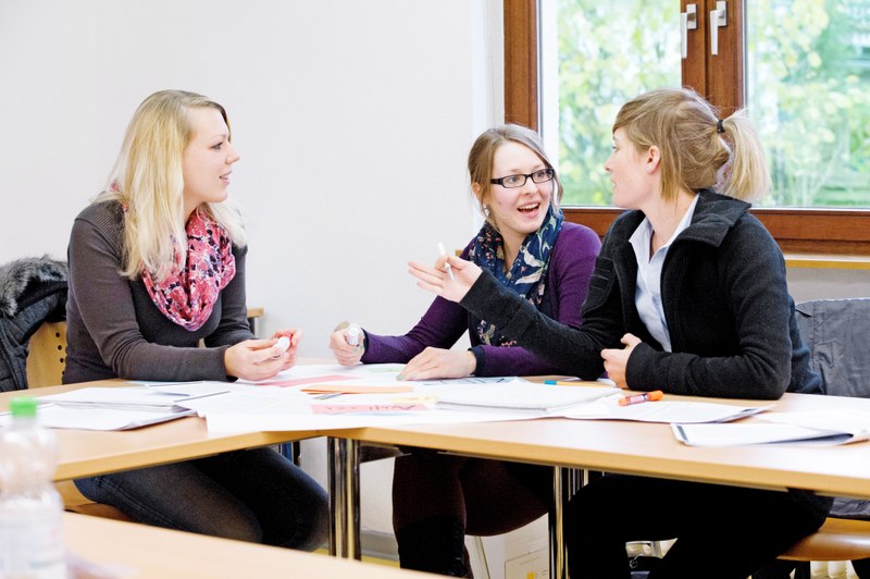 Studierende im Gespräch in einem Seminarraum mit verschiedenen Dokumenten vor sich auf den Tischen.