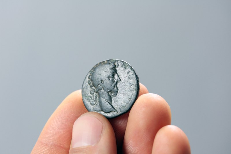 Eine Hand hält eine alte silberfarbene Münze mit Prägung eines Kopfes.