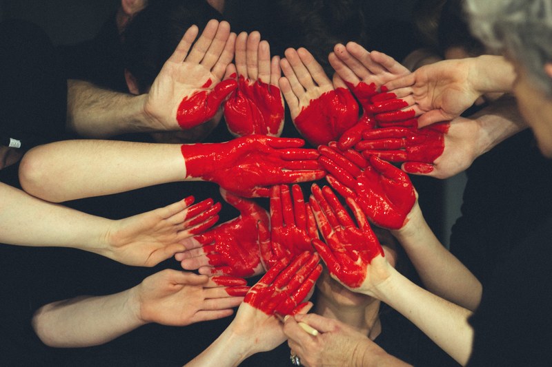 Auf die Handflächen verschiedener Menschen ist ein großes rotes Herz gemalt.