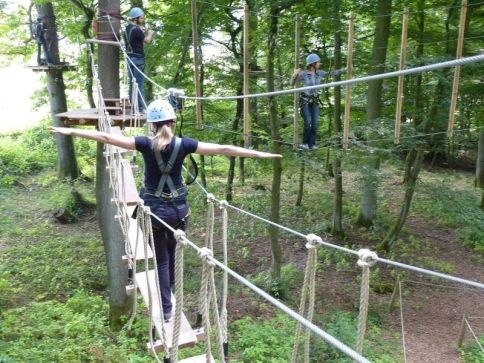 Menschen, die auf einer Wackelbrücke im Kletterwald balancieren